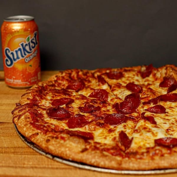 A pepperoni pizza with melted cheese and a Sunkist orange soda can on a wooden surface.