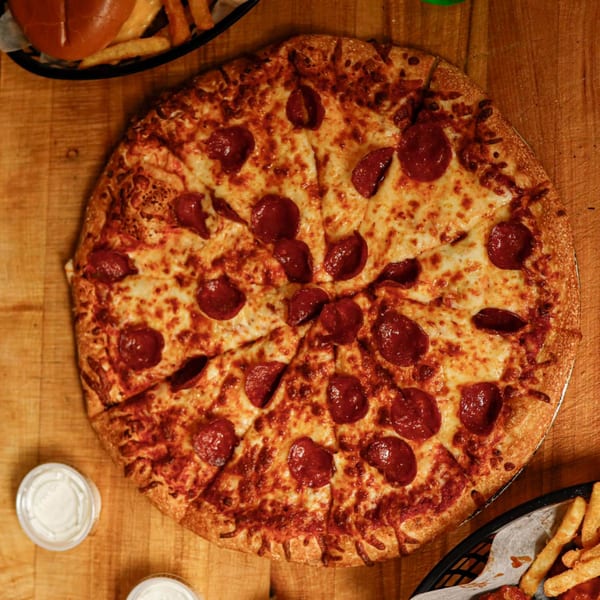 A whole pepperoni pizza, sliced, with a side of fries and dipping sauce on a wooden table.